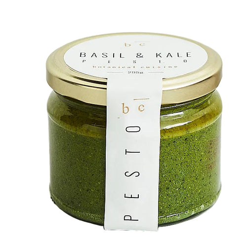 Jar of basil and kale pesto with a gold lid and white label on a white background