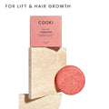 Cooki Shampoo Bar in Cinnamon scent, shown with its pink packaging box and the round pink shampoo bar itself, styled on a white background.