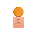 A round orange jasmine shampoo bar sits on top of a peach-colored COOKI box labeled 'JASMINE' against a warm cream background.