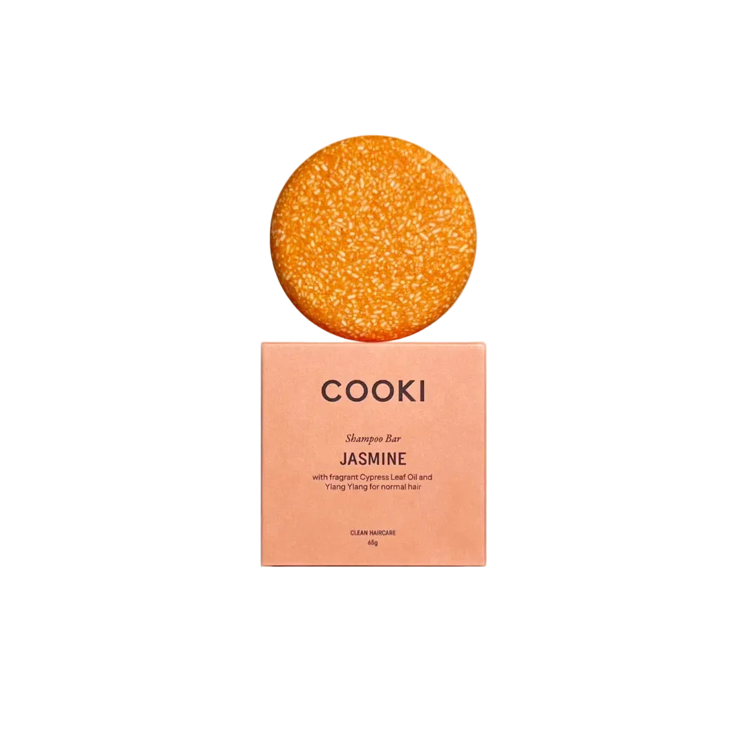 A round orange jasmine shampoo bar sits on top of a peach-colored COOKI box labeled 'JASMINE' against a warm cream background.