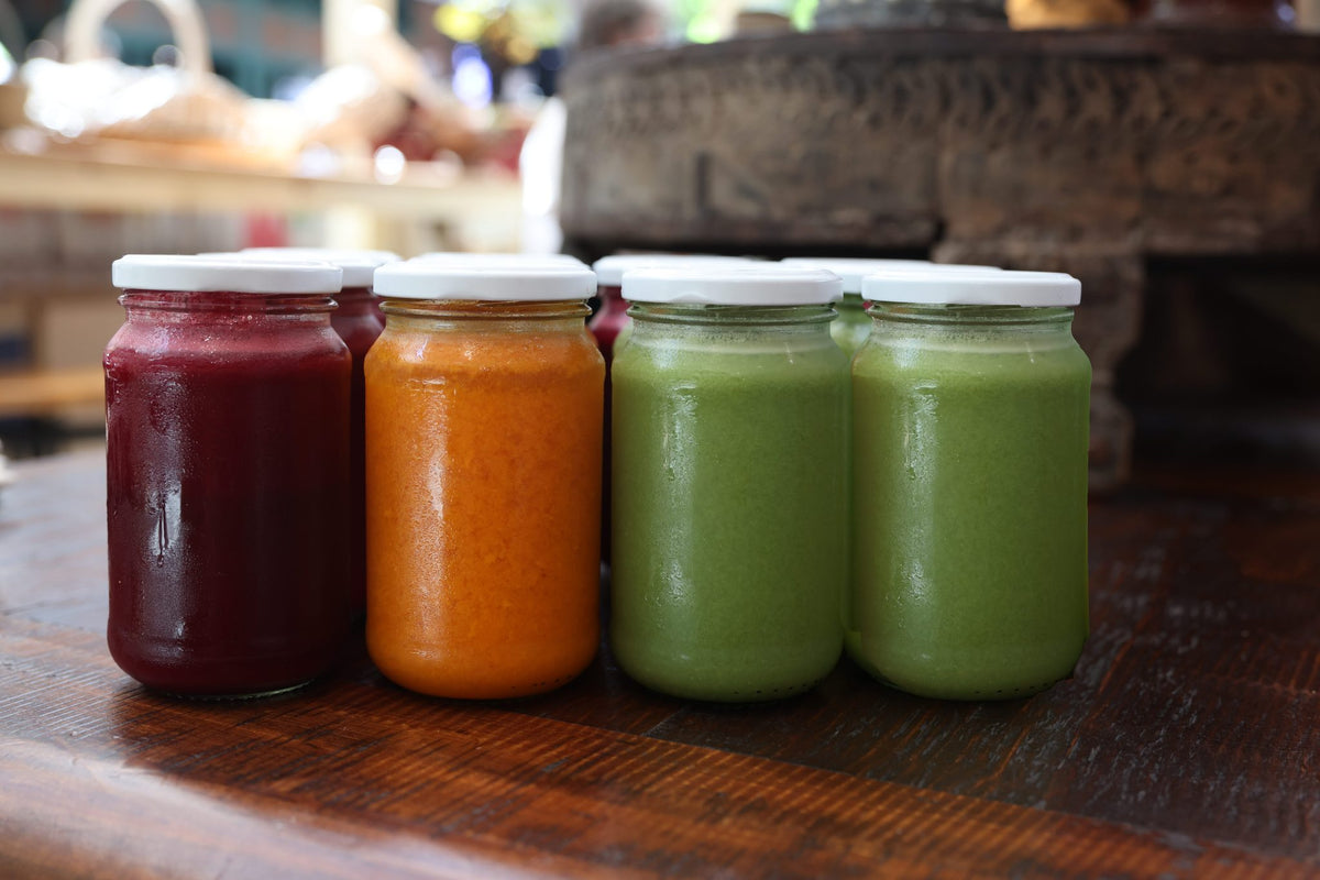 Jars of Greensmith Kitchen organic juice in red, orange and green, lined up on the timber counter.